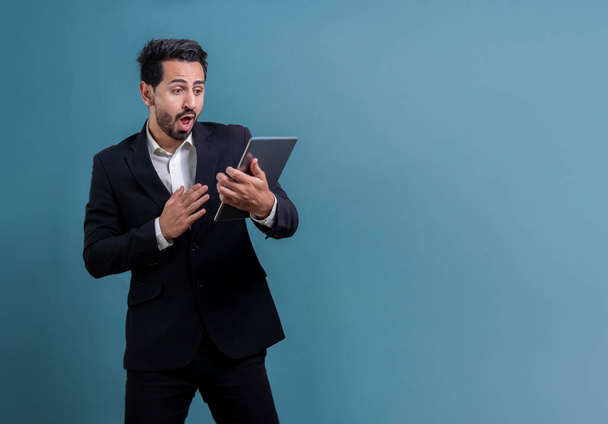 Confident businessman in formal suit holding tablet with surprise look for promotion or advertising. Facial expression and gestures indicate excitement and amazement on an isolated background. Fervent - Fotoğraf, Görsel