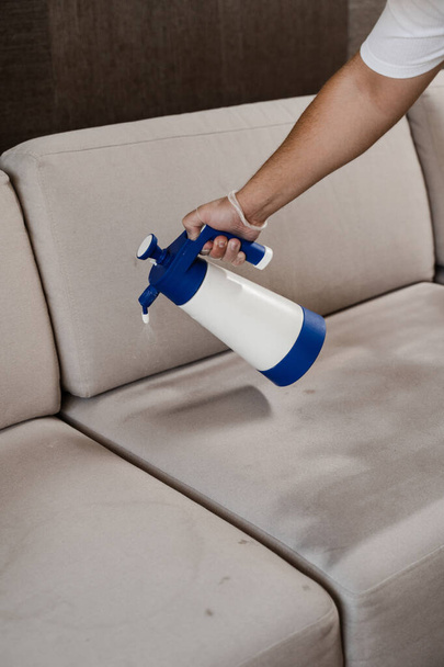 Spraying detergent on couch for dry cleaning using extractor machine. Process of dry cleaning for removing stains and dirt from couch at home. Professional cleaning service - Fotó, kép