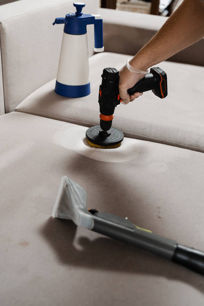 Étaler le détergent sur le canapé à l'aide d'une perceuse avec brosse pour le nettoyage à sec. Appliquer du détergent sur le canapé à l'intérieur de la maison pour le nettoyage à sec - Photo, image