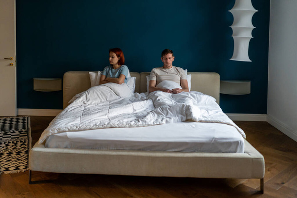 Frustrated sad couple sit on bed under blanket think of relationship problems. Tired offended woman after quarrel lost in thoughts ignores boyfriend with crossed arms. Disappointed lovers in bedroom - Valokuva, kuva
