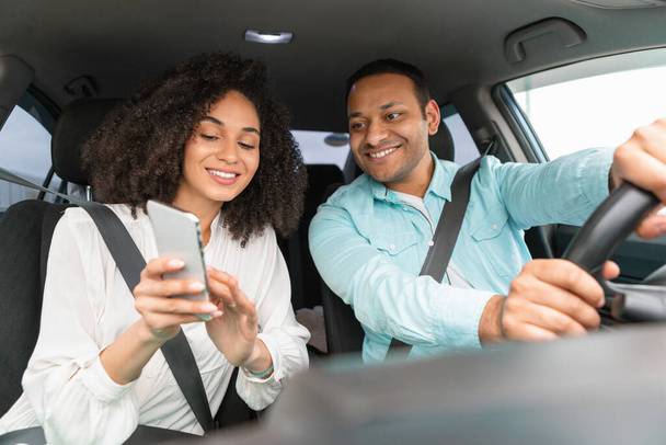 Navigation Concept. Cheerful arabic couple using GPS app on phone for direction and route planning during a drive. Spouses driving new vehicle together navigating via smartphone - Photo, Image
