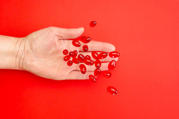 Krill oil capsules in a hand on a red background .omega fatty acids.Healthy eating and food supplements. Flying gelatin red krill oil capsules. Dietary supplements and food supplements - Photo, Image