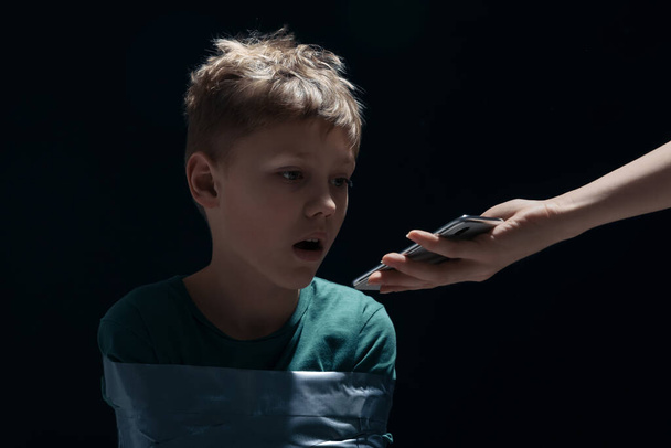 Kidnapper with phone near little boy taken hostage on dark background - Fotoğraf, Görsel