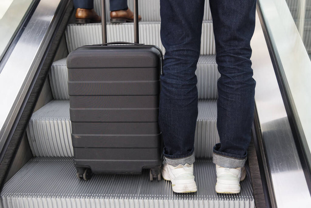 legs of a person with a wheeled suitcase on an escalator - Fotoğraf, Görsel