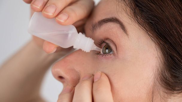 Mujer caucásica goteando gotas hidratantes en sus ojos - Foto, imagen