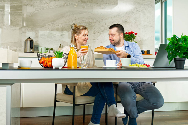 Young beautiful caucasian couple sitting at table while having breakfast at home Happy couple having breakfast together before leaving to work - Foto, imagen