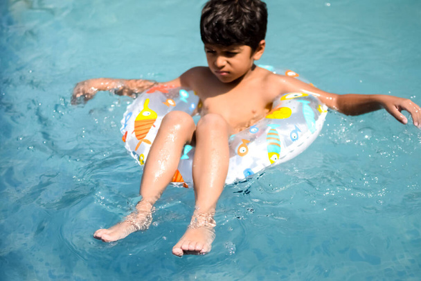 Happy Indian boy swimming in a pool, Kid wearing swimming costume along with air tube during hot summer vacations, Children boy in big swimming pool. - Foto, afbeelding
