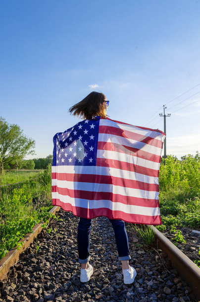 Rückansicht einer Frau mit einer amerikanischen Flagge im Freien. Junge Frau mit amerikanischer Flagge. Feierlichkeiten zum Unabhängigkeitstag der USA.  - Foto, Bild