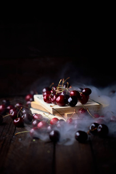 Cherries on top of old books with a layer of thick white smoke on a wooden background - Foto, Imagem