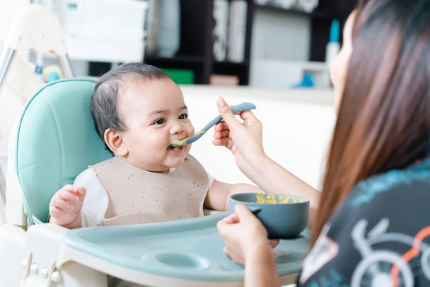 Baby enjoy and eating porridge in high chair. - Фото, изображение