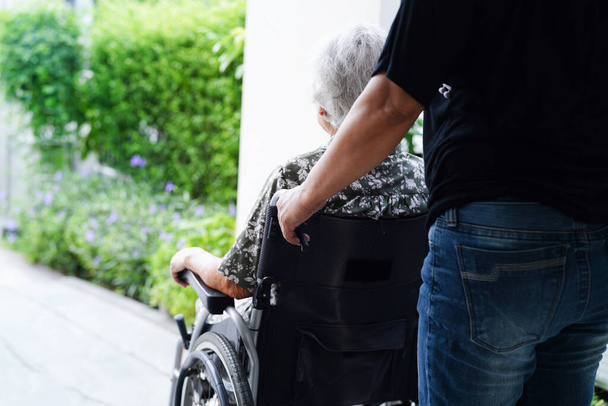 Доглядальниця допомагає азіатській жінці з інвалідністю сидіти на інвалідному візку в лікарні, медична концепція.       - Фото, зображення