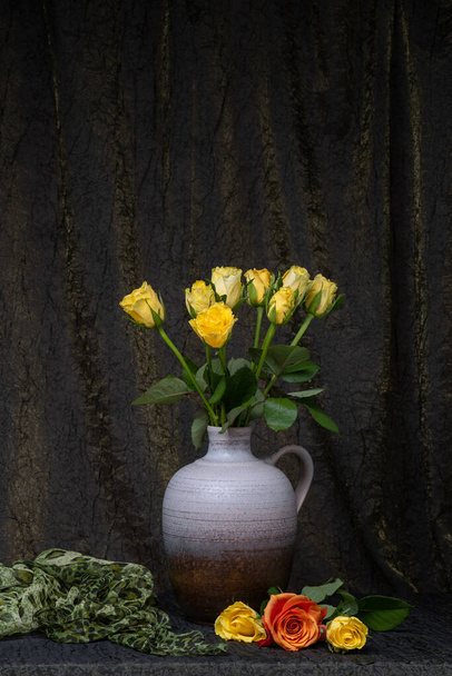Kytice žlutých růží ve váze, džbán. Tmavá tkanina pozadí. Nedaleko jsou tři růže. Místo pro nápis. květina zátiší - Fotografie, Obrázek