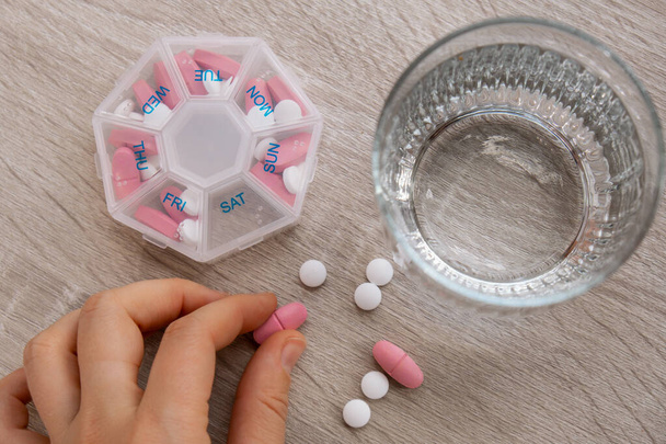 Vrouw sorteerpillen Organizer wekelijkse shots Sluiten van medische pil doos met doses tabletten voor dagelijks gebruik neem medicijnen met witte roze drugs en capsules. Jonge vrouw krijgt haar dagelijkse vitaminen thuis - Foto, afbeelding