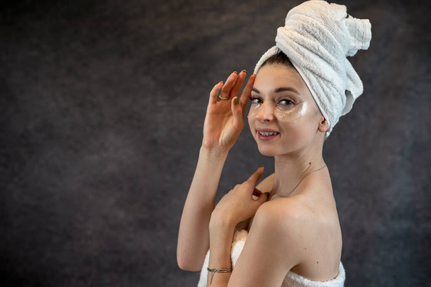 Beauty woman in towel applies black collagen patches under eyes isolated on black.  Skincare, anti fatigue eye mask - Photo, Image