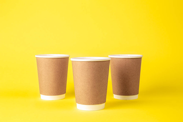 Tre tazze monouso di carta su uno sfondo giallo isolato. Eco concept, senza plastica. - Foto, immagini