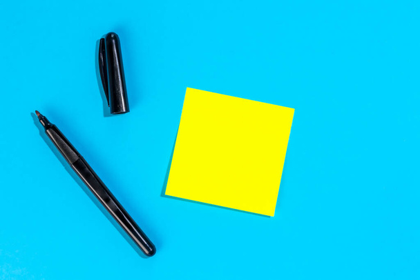 Nota gialla con spazio vuoto per il testo con pennarello su sfondo blu, posa piatta. Concetto promemoria. - Foto, immagini