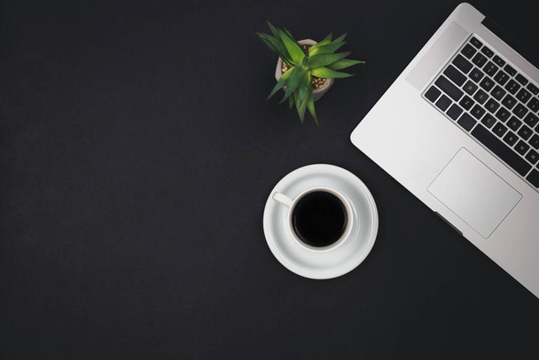 Laptop, coffee cup and office plant on black background, top view, copy space. - Photo, Image