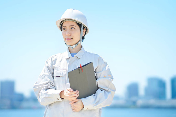 Una donna che indossa un casco e indossa abiti da lavoro in bella giornata - Foto, immagini