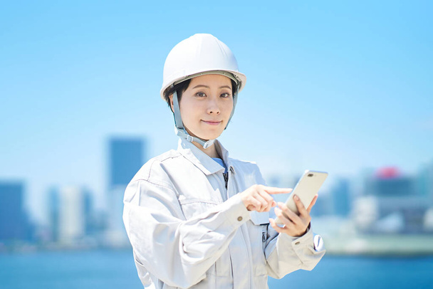 A woman in work clothes holding a smartphone on fine day - Foto, afbeelding