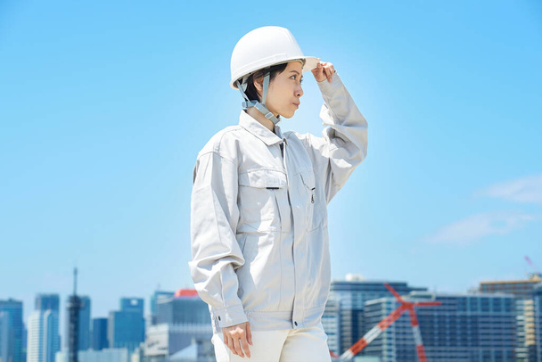 A woman wearing work clothes and checking a helmet on fine day - Foto, immagini