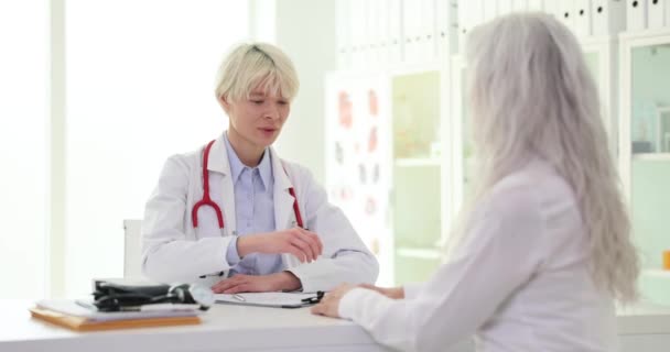 Une femme âgée consulte un médecin et reçoit des nouvelles optimistes après un examen médical. Thérapeute tenant la main d'un vieux patient - Séquence, vidéo
