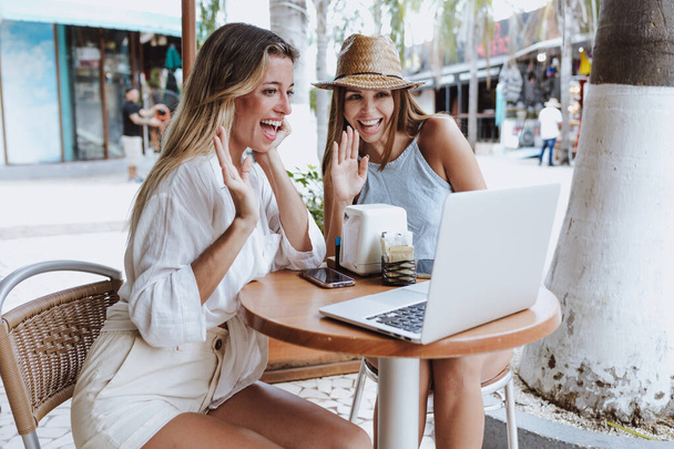 young latin couple of women friends using laptop and drinking coffee at restaurant terrace for video conference in Mexico Latin America, hispanic people in caribbean city with tropical background - Foto, afbeelding