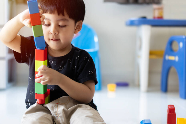 Παιδί ασιατικό χαριτωμένο αγόρι παίζει δημιουργικό μπλοκ παιχνιδιών στο σπίτι. Τα δημιουργικά παιδιά του νηπιαγωγείου χτίζουν έναν πύργο. Εκπαιδευτικά παιχνίδια για νήπια ή βρέφη. - Φωτογραφία, εικόνα