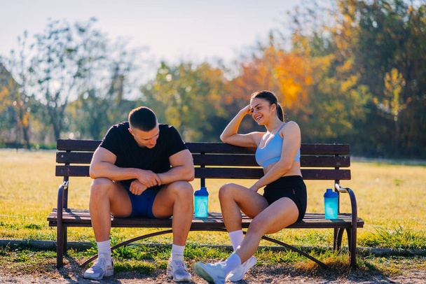 Cansada pareja deportiva teniendo una conversación mientras descansa en el banco - Foto, imagen