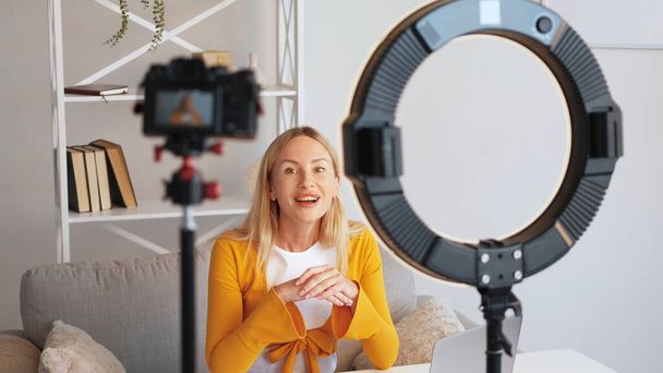 Creating video content. Online speaker. Shooting vlog. Friendly smiling woman influencer filming blog using camera tripod ring light home interior. - Foto, afbeelding