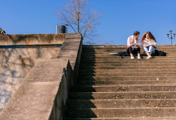 Long distance view of high school girls sitting on a staircase, studying together - 写真・画像