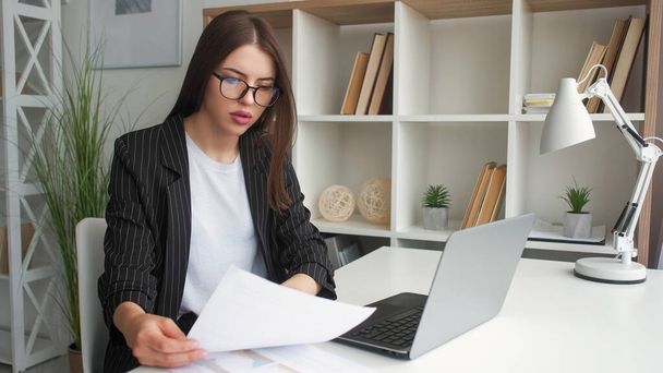 Freelance paperwork. Remote job. Serious executive woman working online with laptop and documents making report at home office workplace. - Φωτογραφία, εικόνα