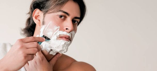 Shaving face. Morning grooming. Attractive concentrated brown haired guy using facial foam razor isolated on white copy space background. - Fotó, kép