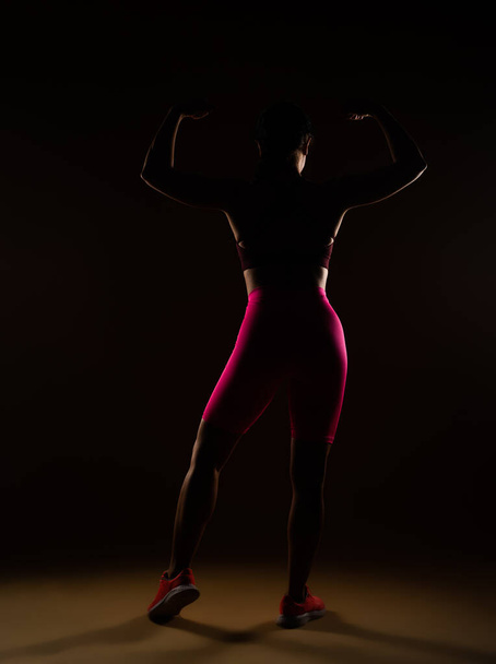 Widok z tyłu zdjęcie silnej kobiety pozującej w studio na beżowym tle. Zdjęcie sylwetki - Zdjęcie, obraz