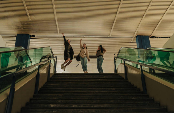 Three happy girls jumping before they go downstairs at the shopping center - Zdjęcie, obraz