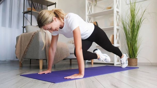Home sport. Indoor workout. Powerful hardy woman fitness training plank running exercising beautiful perfect body domestic interior. - Photo, image