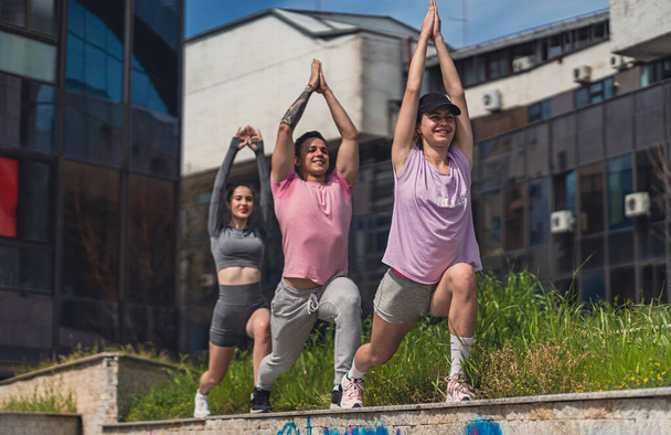 Low angle view shot of three fit sports friends working out while dangerously standing on a wall ledge - Fotografie, Obrázek