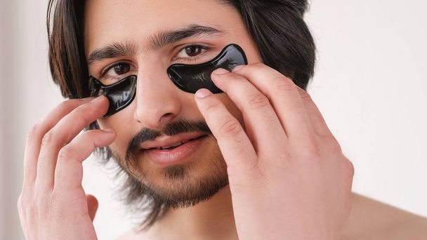 Eye patches. Male grooming. Skincare cosmetology. Attractive guy applying hydrogel black pads on face isolated on white copy space background. - Foto, Imagem