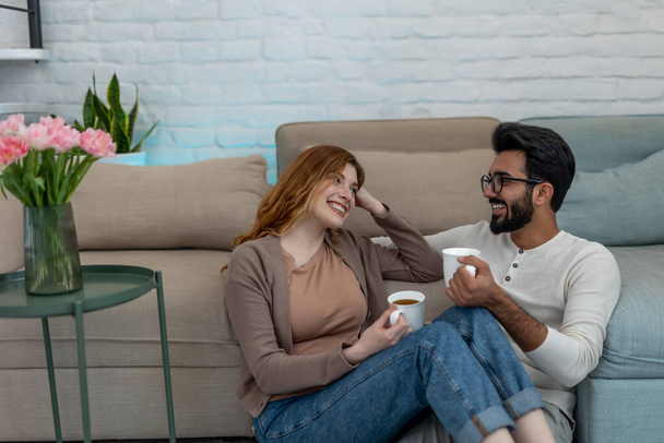 Affectionate loving married couple drinking coffeee, enjoying spending time together at home in cosy living room, relaxing, sweet tender moment. - Фото, зображення