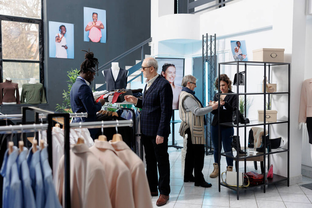 Afro-amerikan çalışanlar müşterilerine resmi kıyafet için yardım ediyor, elbise mağazasında kravat kumaşlarını kontrol ediyor. Üst düzey müşteri modern butikte gündelik kıyafet ve şık aksesuarlar alıyor. - Fotoğraf, Görsel