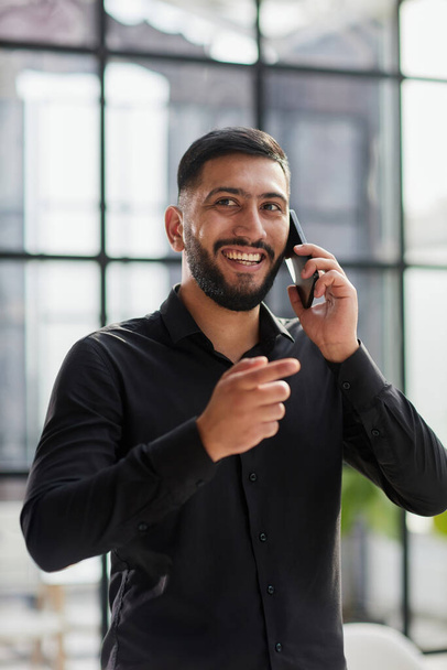 young man in a black shirt talking on the phone in the office - Foto, afbeelding