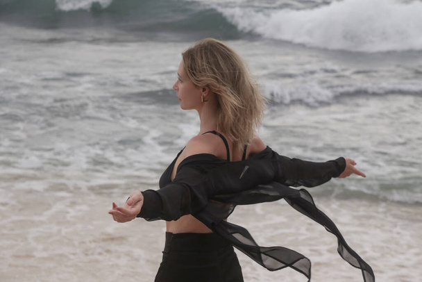 Issız okyanus sahillerinde siyah elbiseli genç bir kadının portresi, özgürlük kavramı ve harita dışı seyahat. - Fotoğraf, Görsel