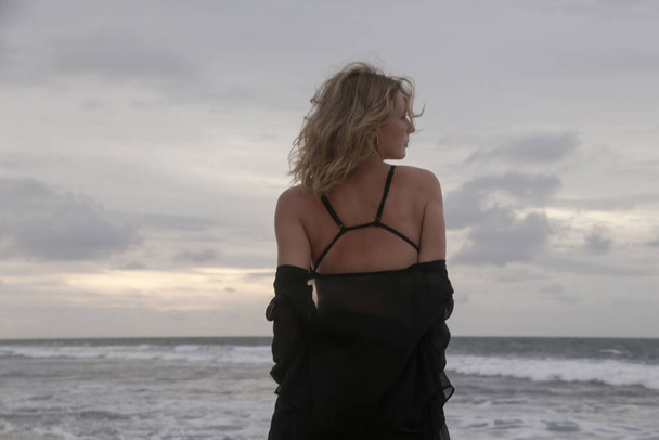 Retrato de una joven vestida de negro en la playa isloada del océano vacío, concepto de libertad y fuera del mapa de viaje - Foto, Imagen