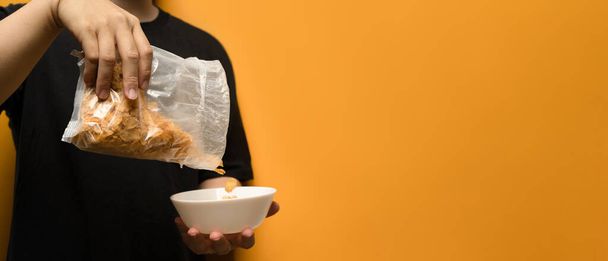 Cropped shot of man pouring cereals into a white bowl isolated on yellow background with space for advertising text message. - Valokuva, kuva