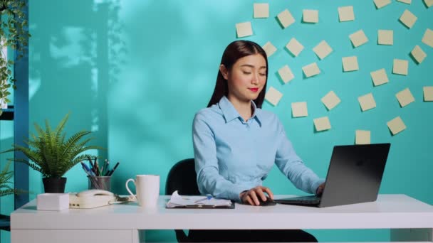 Mutlu Asyalı iş kadını, mavi stüdyo geçmişi üzerinden modern parlak yaratıcı ofis masasına veri yüklüyor. Rahatlamış idari işyerlerine veri yükleyen gülümseyen bir çalışan - Video, Çekim