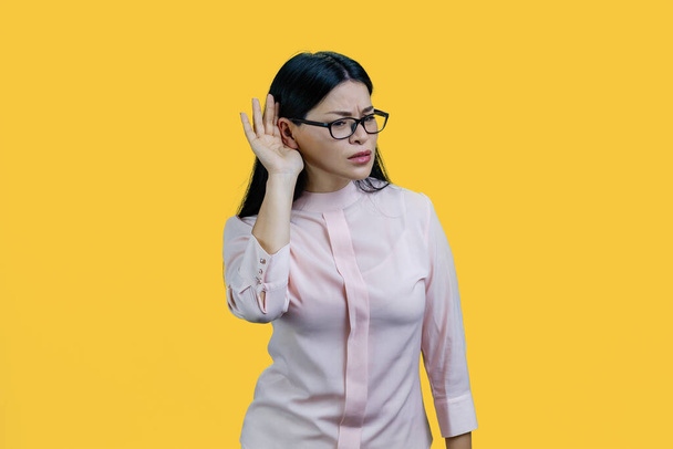 Portrait d'une jeune femme asiatique entendant des commérages. Isolé sur fond jaune. - Photo, image
