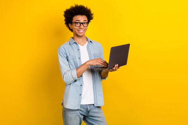 Photo of smart funky guy dressed denim shirt eyewear chatting apple samsung device isolated yellow color background. - Фото, изображение