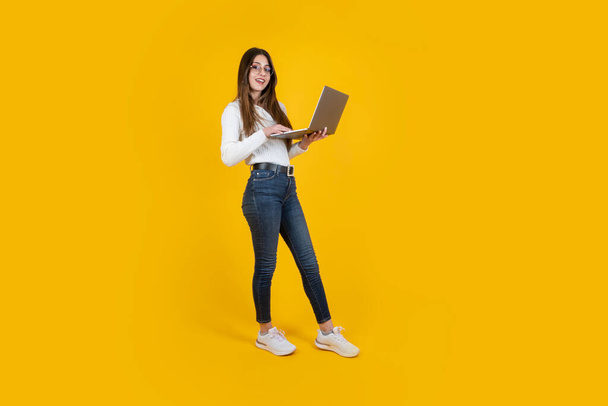 Full length side body view woman holding modern laptop. Young businesswoman wearing  jeans and white shirt. Office worker employee using computer. Caucasian long brown haired beautiful teenage girl. - Фото, зображення