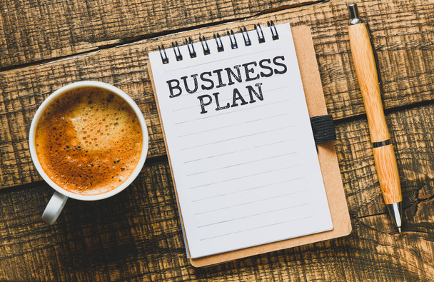 Бизнес-план в офисном блокноте на деревянном столе рядом с кофейной кружкой. - Фото, изображение