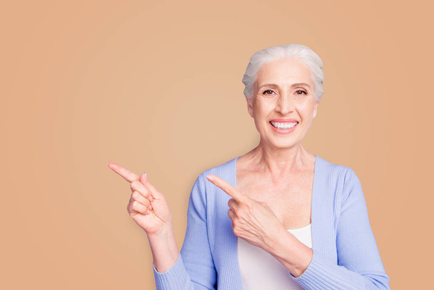 Beautiful nice cheerful smiling gray-haired old lady wearing casual, showing pointing way with two fingers. Copy space. Isolated over pastel violet purple background. - Valokuva, kuva