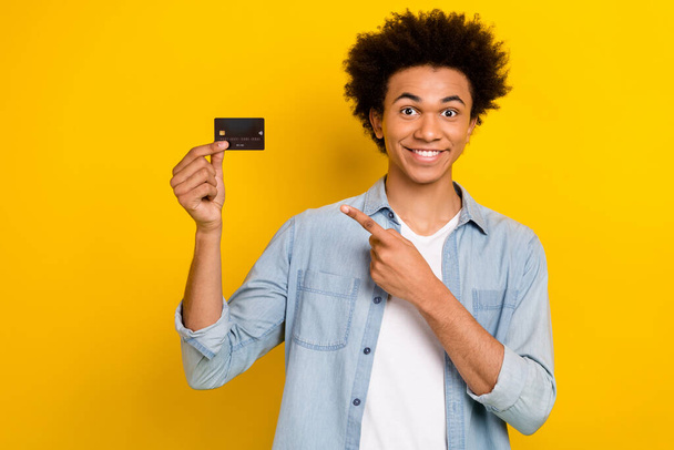 Photo of funky cheerful man wear jeans shirt pointing finger credit card isolated yellow color background. - Photo, Image